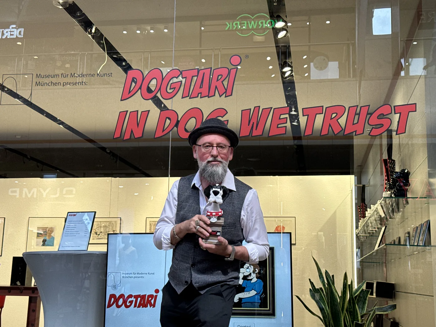 Olaf Neumann mit einer Hundefigur vor dem Schaufenster mit dem Schriftzug DOGTARI IN DOG WE TRUST