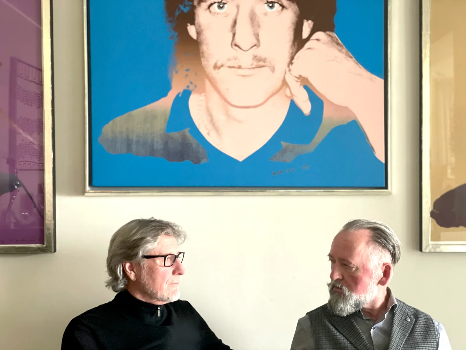 Harald Toni Schumacher und Olaf Neumann sitzen im Gespräch unter dem Warhol-Porträt